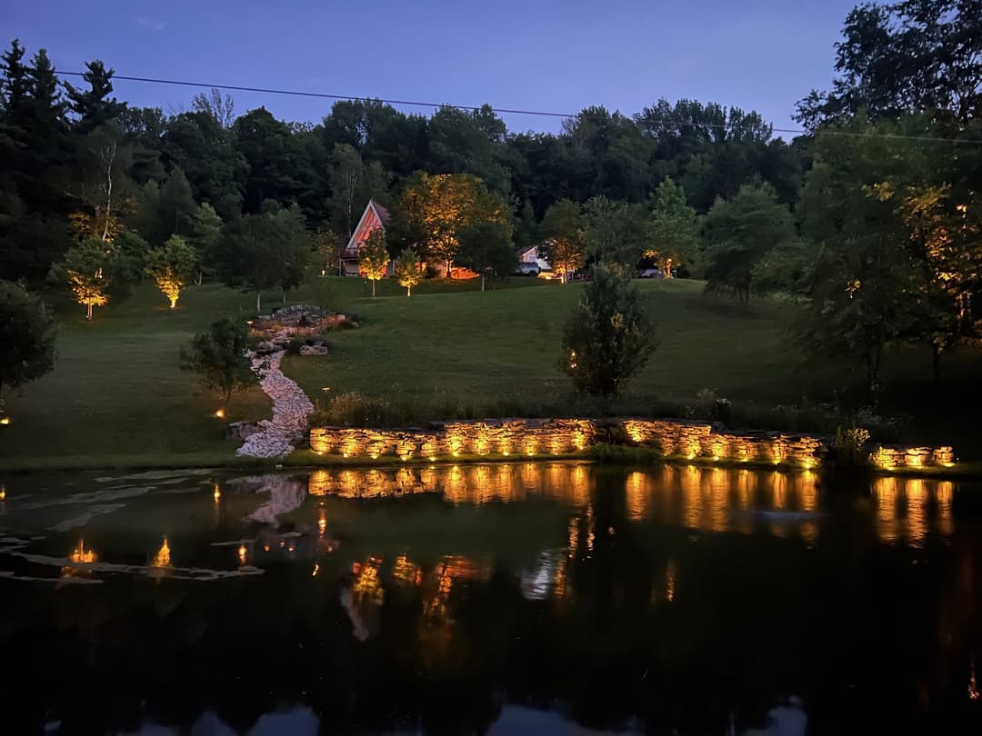 Serene twilight landscape with illuminated trees and a peaceful pond reflecting lights.