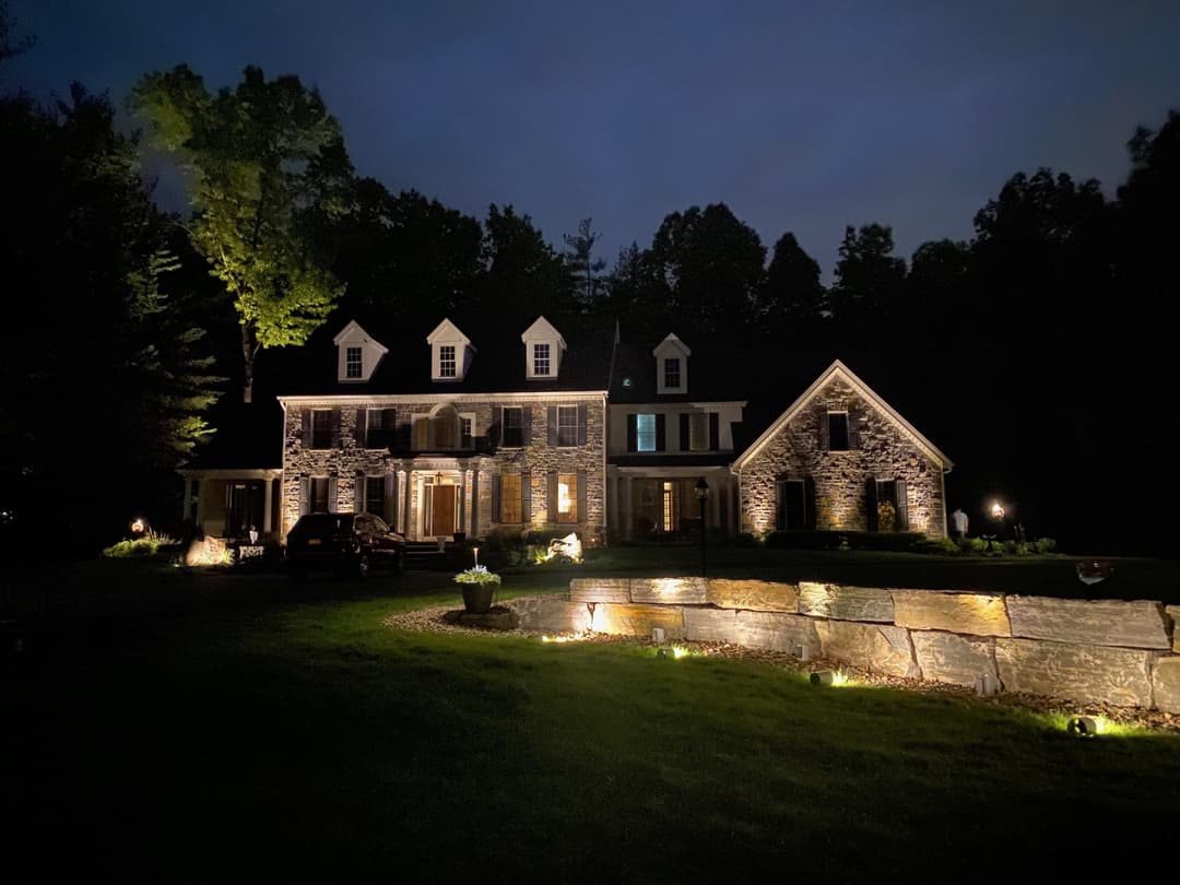 Beautiful stone house illuminated at night, surrounded by trees and landscaped grounds.