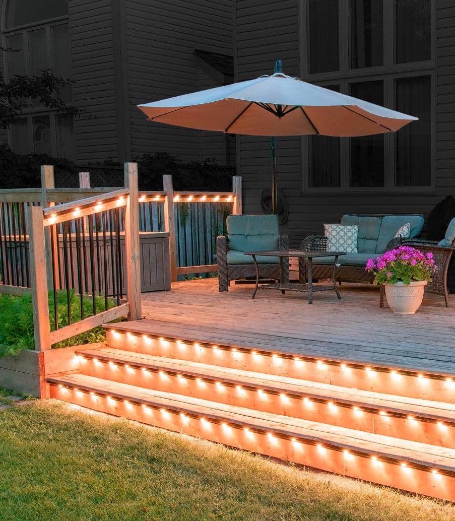 Cozy outdoor deck with string lights, umbrella, seating area, and flower pot.