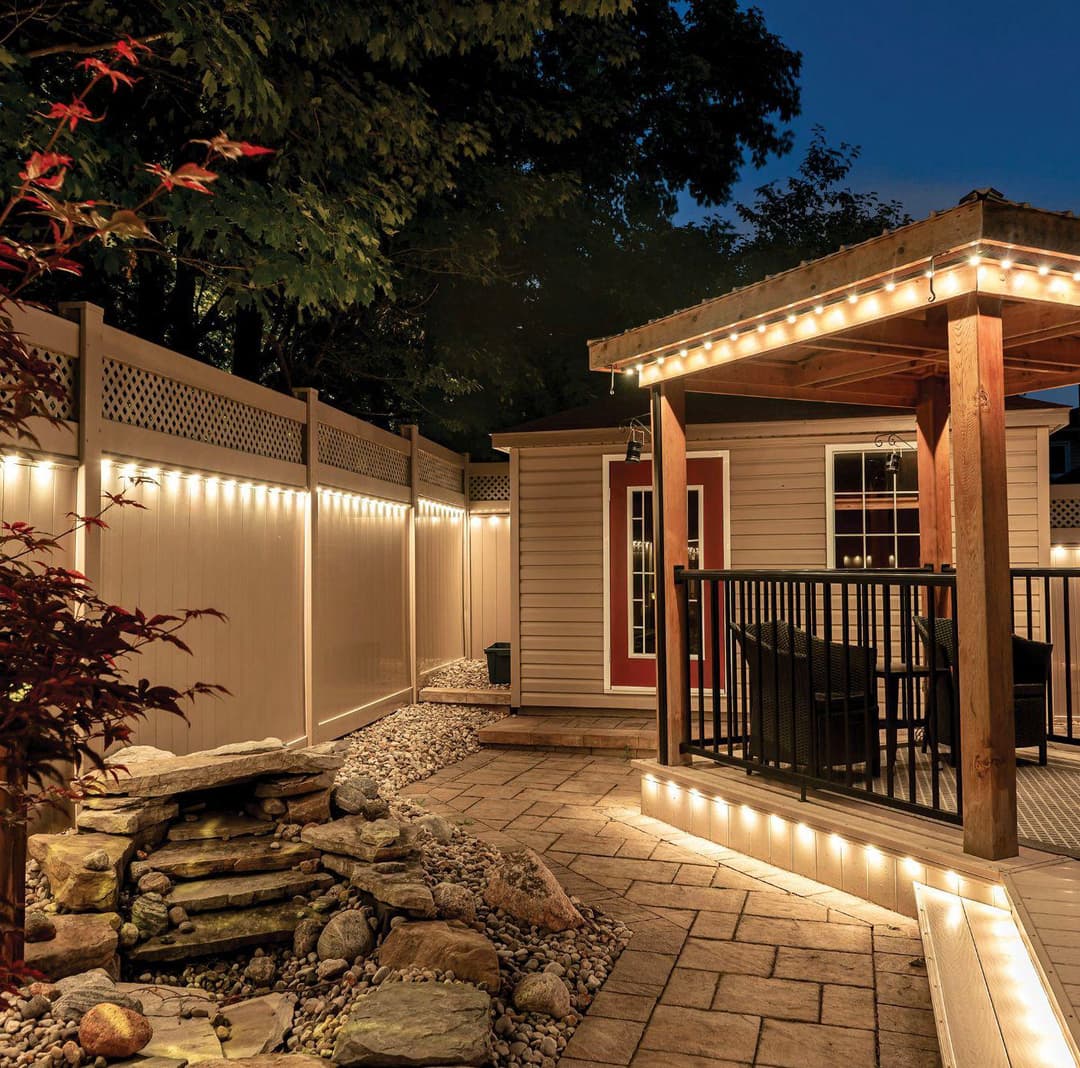 Cozy backyard patio with ambient lighting, pergola, and stone landscaping at dusk.