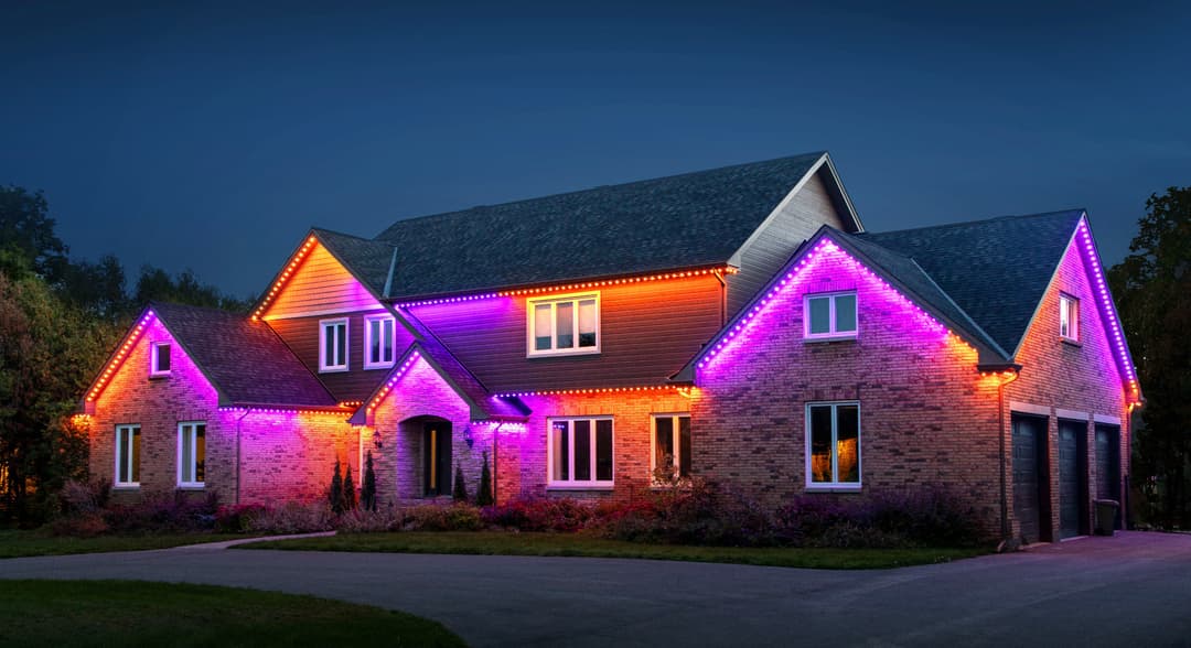 Modern brick house adorned with vibrant orange and purple LED holiday lights at night.